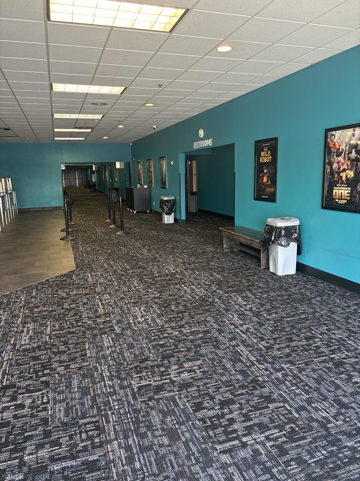 A dimly lit, empty hallway of a movie theater. The walls are painted a vibrant teal, and the floor i 