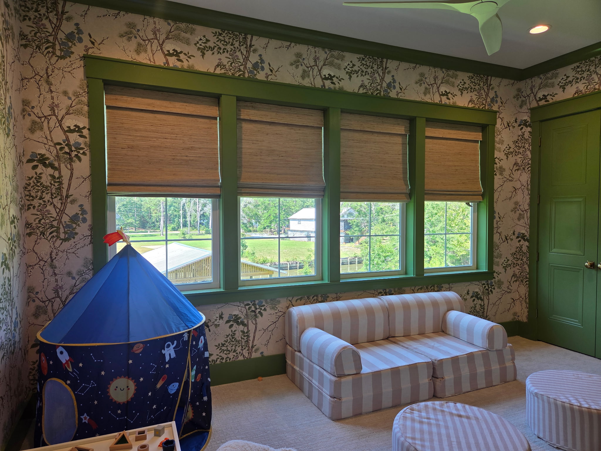 Woven wood shades bring warm texture and soft filtered light to this Mobile playroom window wall. Custom fitted and professionally installed by Budget Blinds of Mobile for a clean inside mount on every panel.
