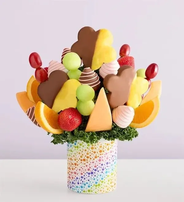 A colorful fruit and chocolate arrangement is presented in a polka-dot cylindrical vase. The bouquet 