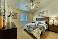 Carpeted bedroom with ceiling fan, small window, and vaulted ceiling.