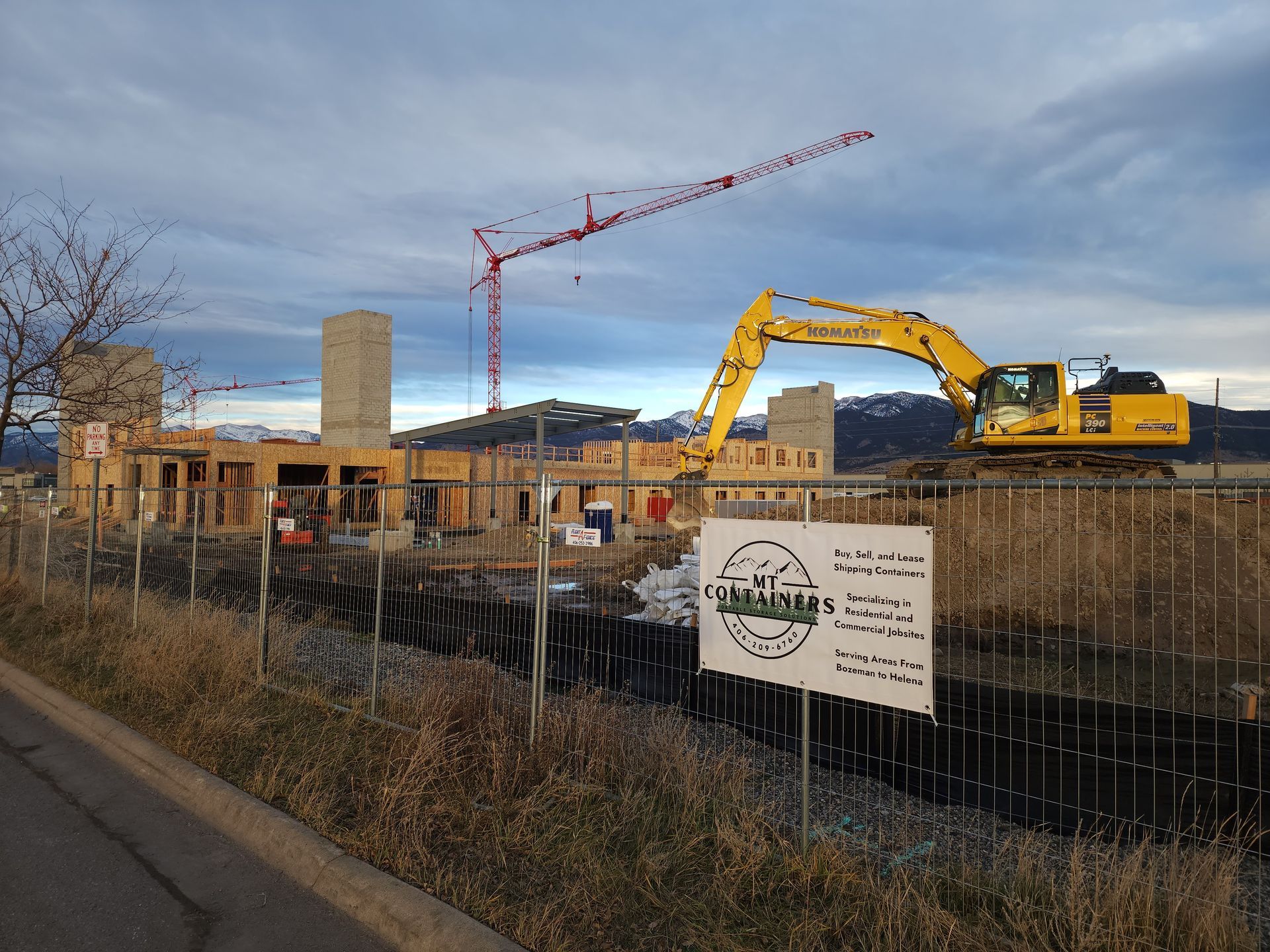 Construction site with crane and excavator working near building structure, featuring portable storage container company signage on fence, highlighting use of storage containers for construction site organization and material storage.