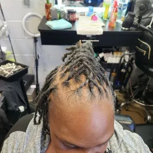 Partially reconstructed starter locs secured into a top section, featuring clean scalp lines and pro 