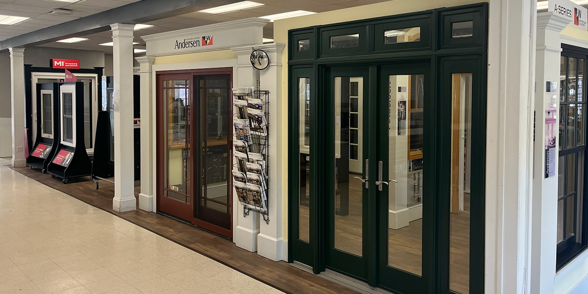 A display of Andersen doors at Builders FirstSource in Oxford, CT, showcasing various styles and designs, including a green double-door option and a mahogany-colored door with glass panels.