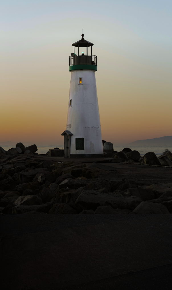 A lighthouse on a rocky oceanside outpost, pictured at dusk.