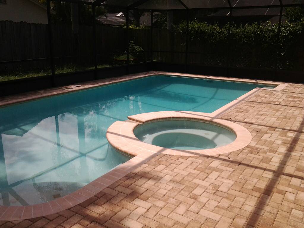 Custom swimming pool with an integrated round spa and surrounding brick paver patio.
