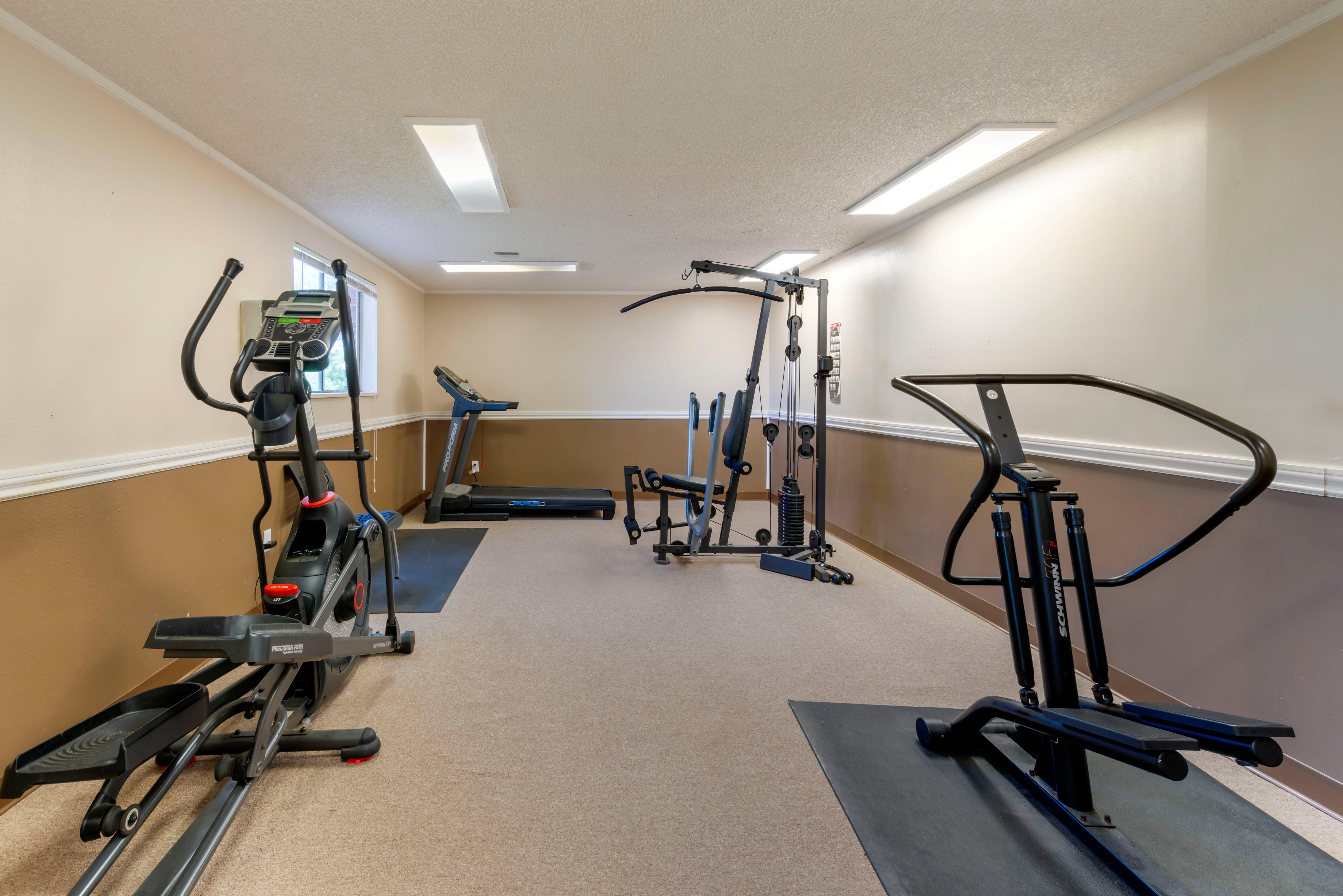 Carpeted fitness center with cardio machines, weight machines, and a treadmill.